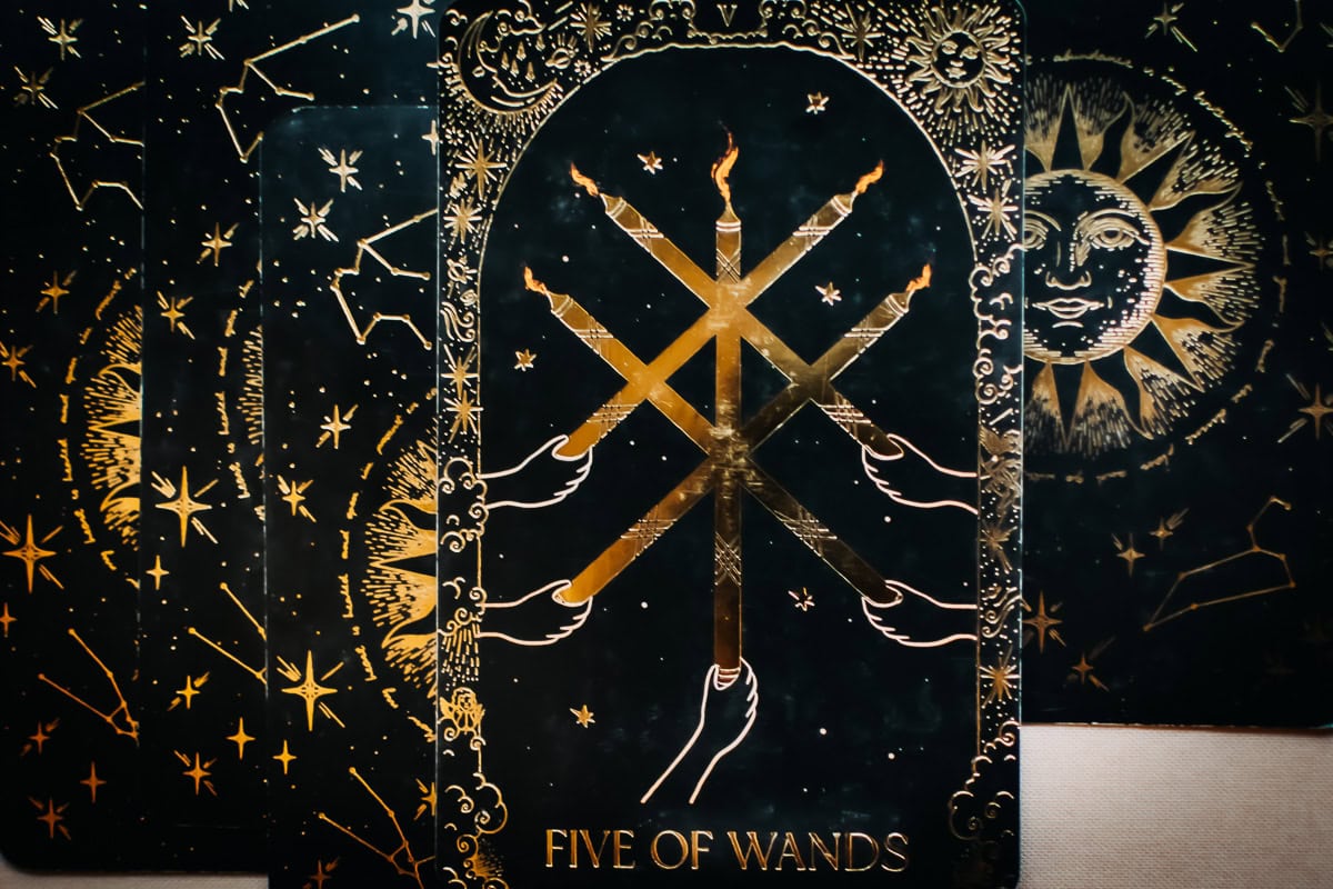 The Five of Wands card depicted emotionally by 5 wands set afire. 