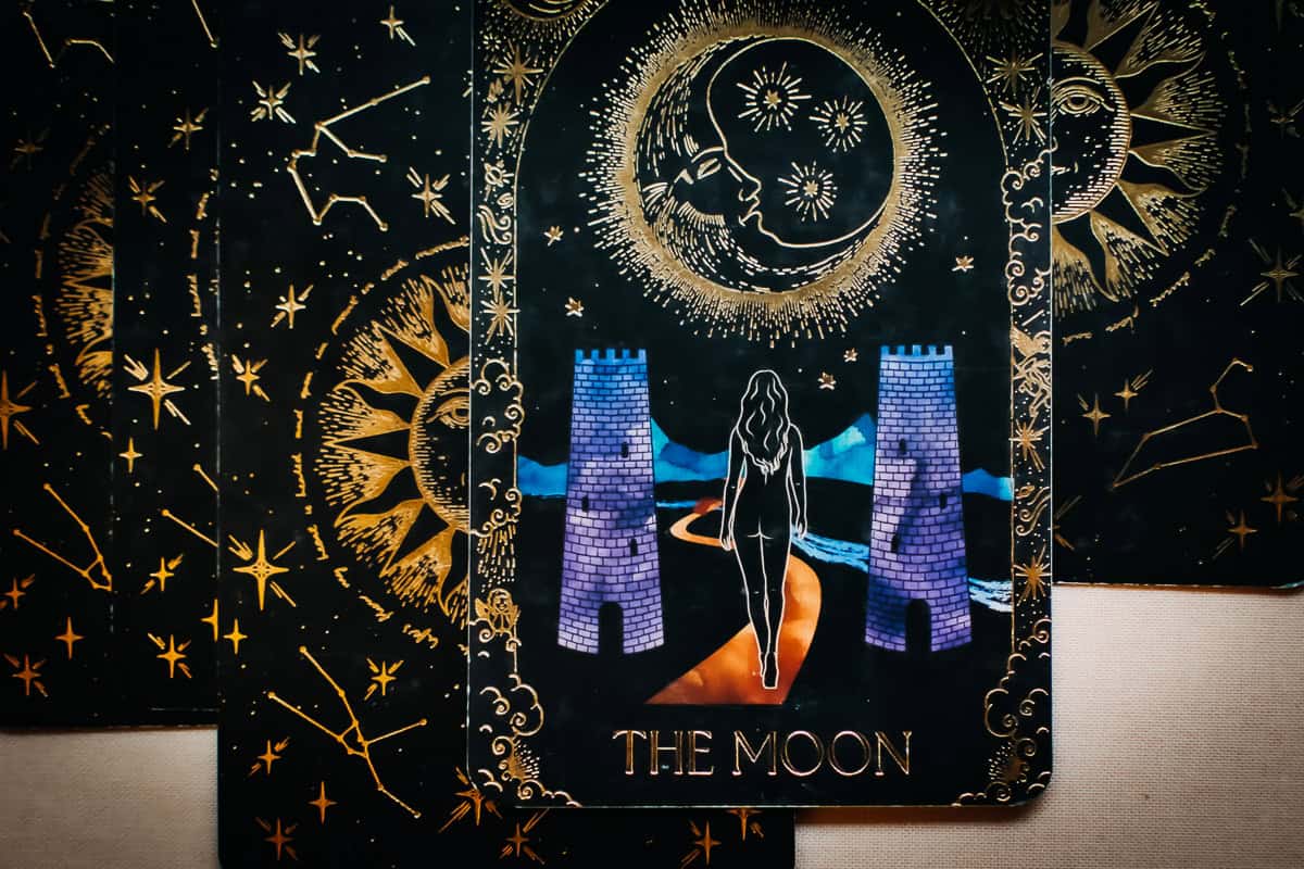 The Major Arcana card of The Moon shown as feelings depicting a woman walking under a glowing moonlight between two towers. 