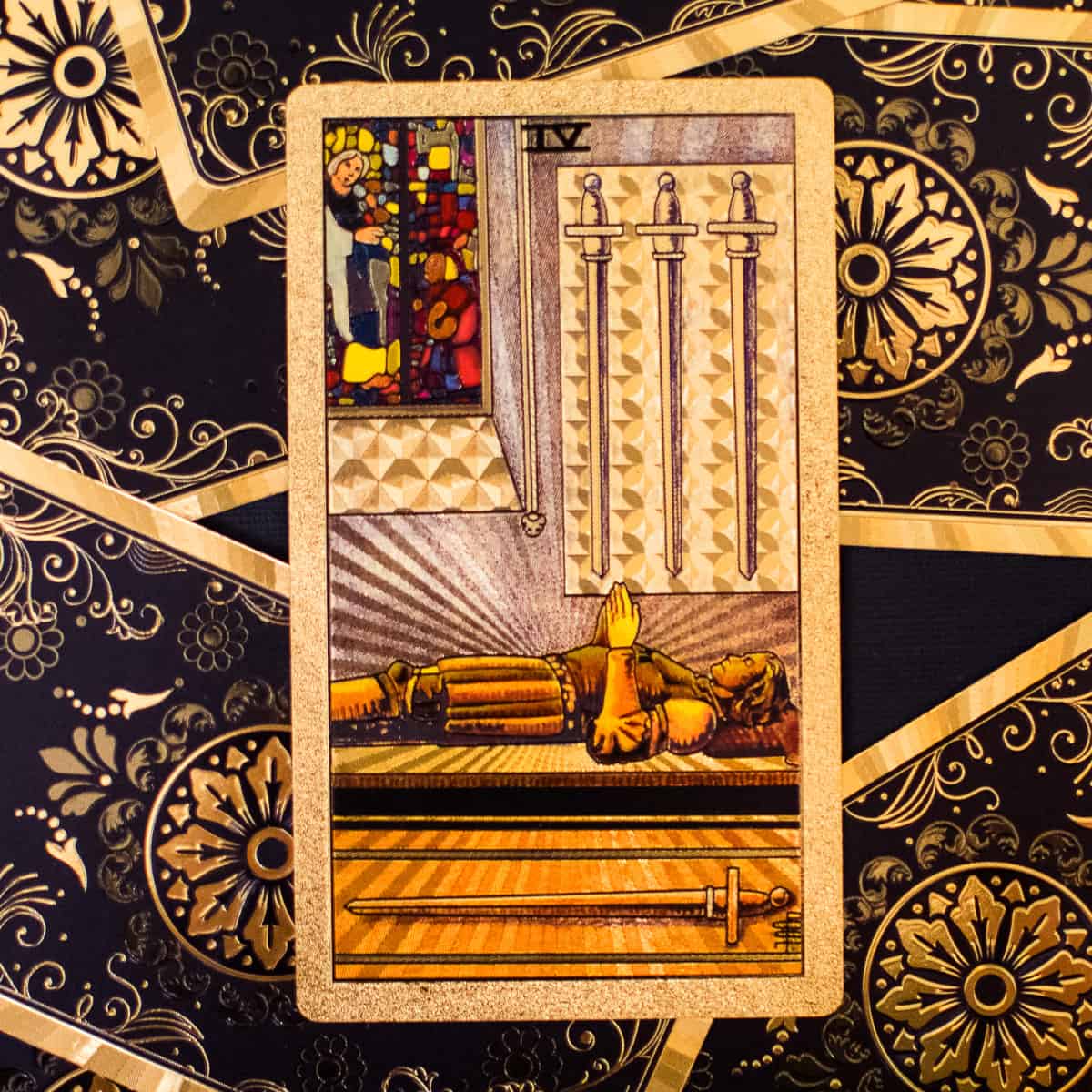 A person in deep sleep on a table surrounded by 4 swords on a tarot card.