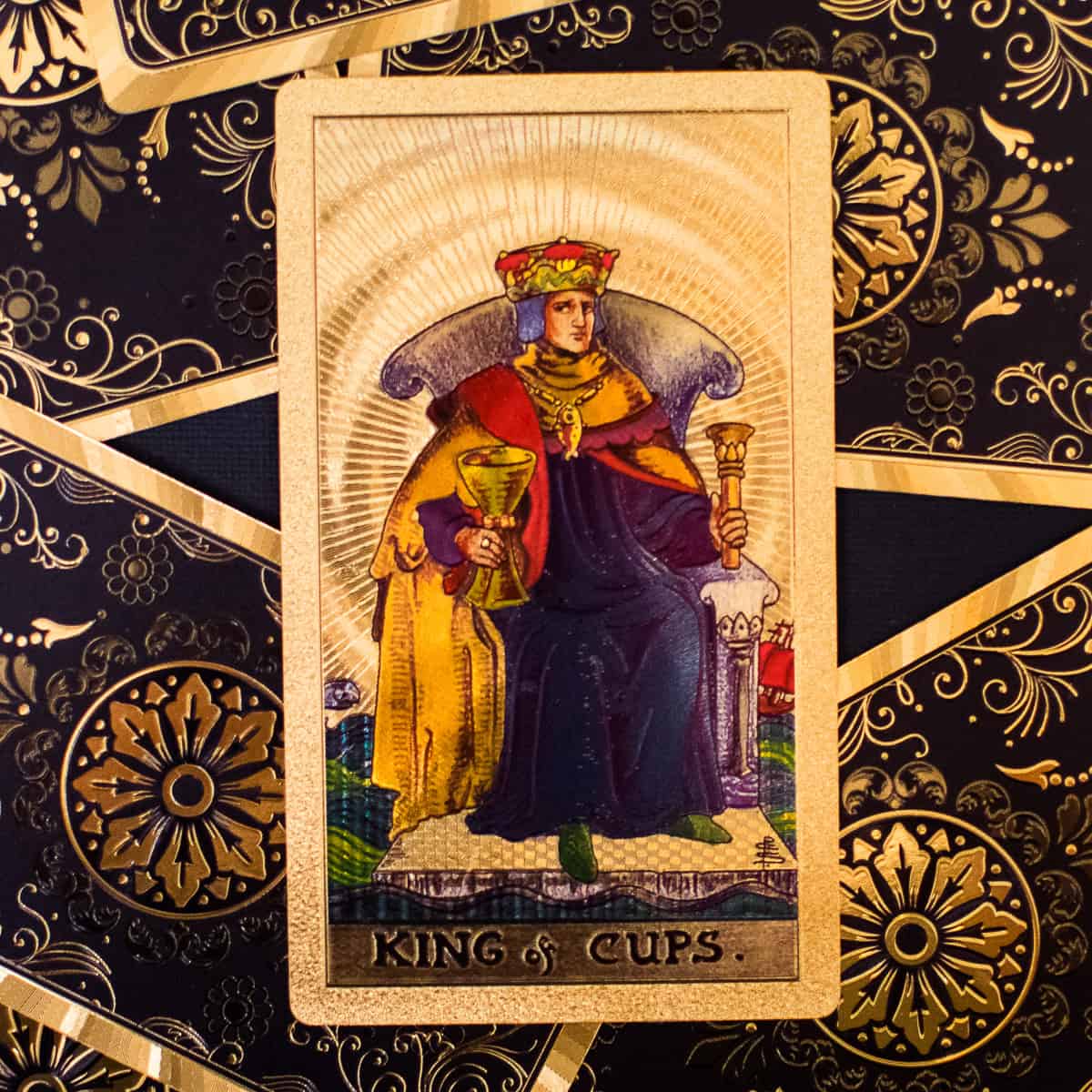 A king sitting on a throne holding a golden cup on a tarot card.