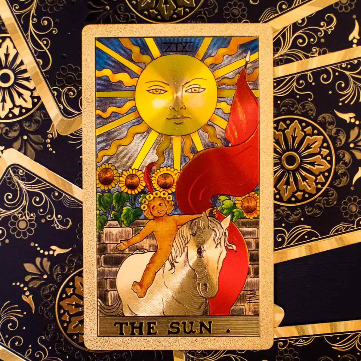 Sun with a face over a child with red cape on a white horse depicted on a tarot card.