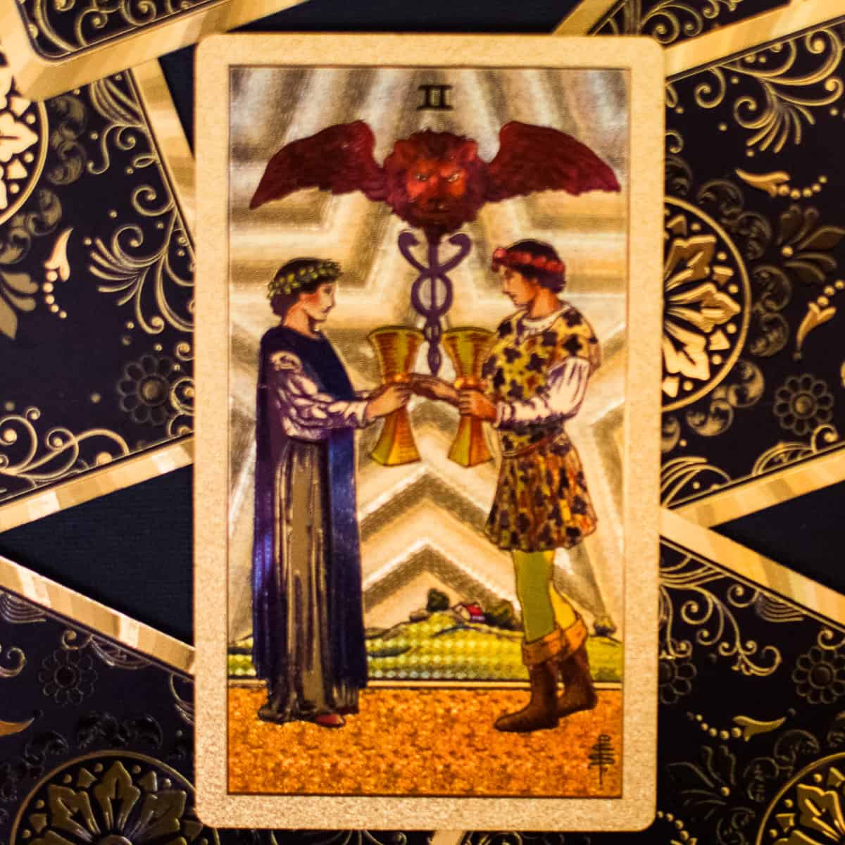 A man and woman exchanging gold cups depicted on a tarot card.