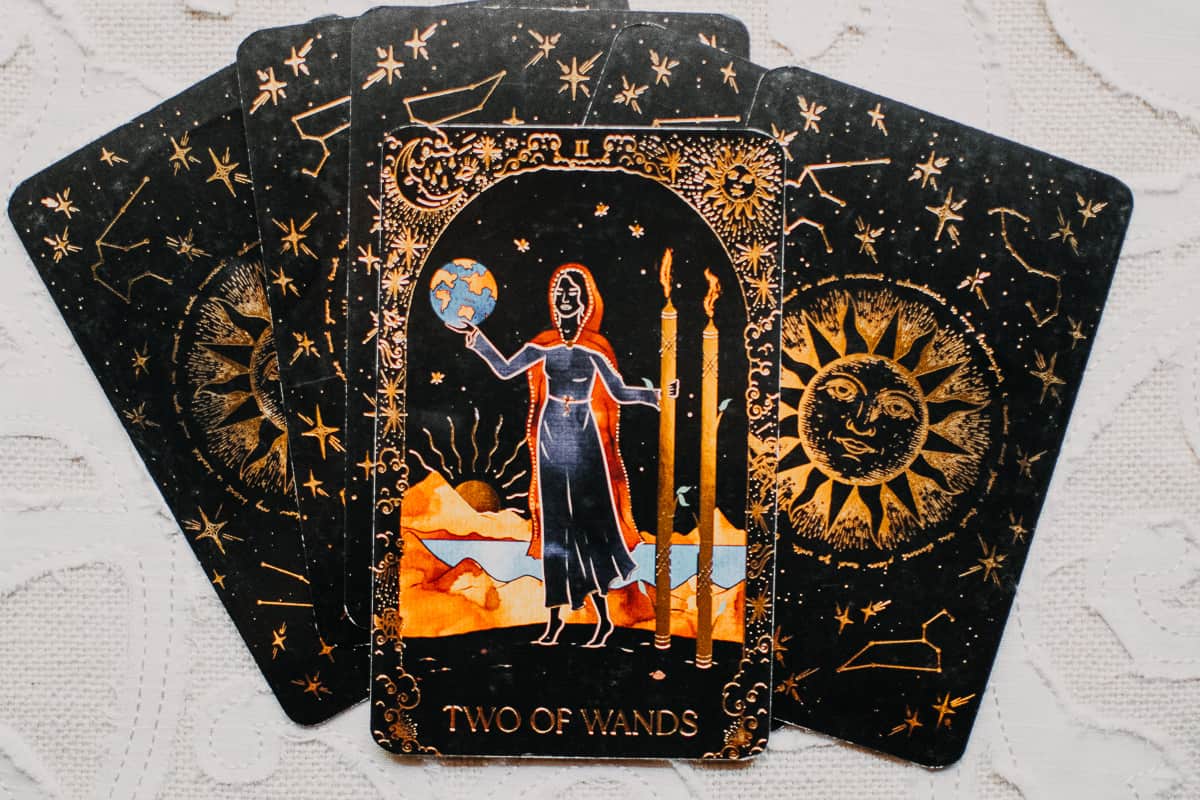The Two of Wands tarot card by Dreamy Moons on a stack of tarot cards. 