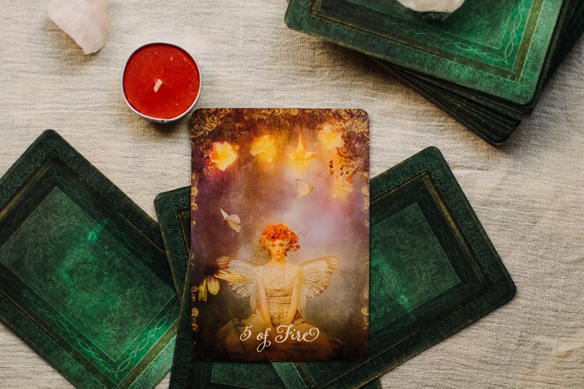 The Five of Wands card depicting a fairy under 5 glowing floral orbs. 
