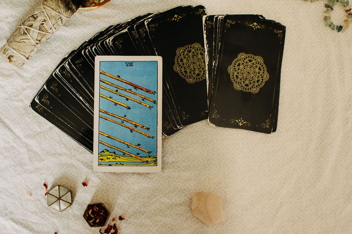 The Eight of Wands tarot card alongside sage and rose quartz.