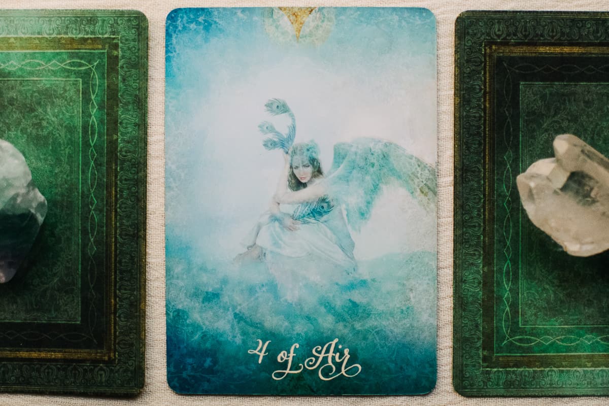 The Four of Air (Swords) card between two other tarot cards with crystals on them.