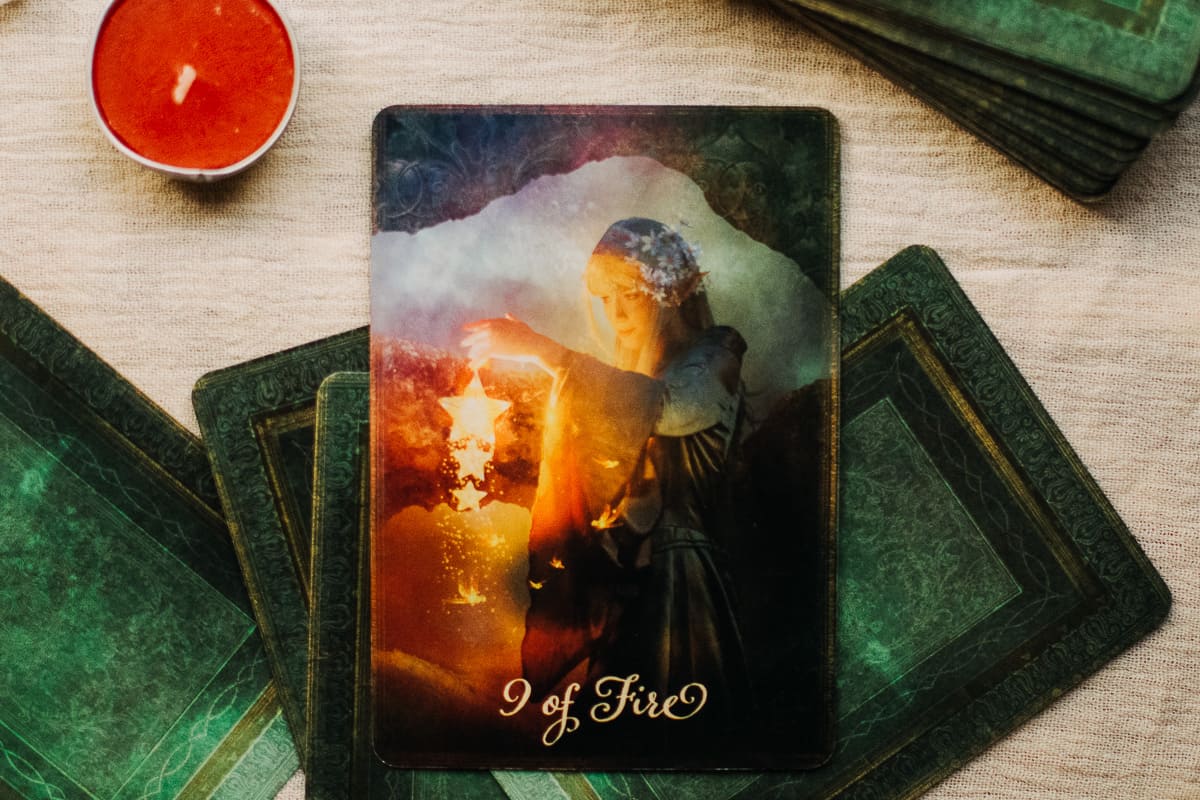 The 9 of Fire tarot card surrounded by a candle and crystal. 