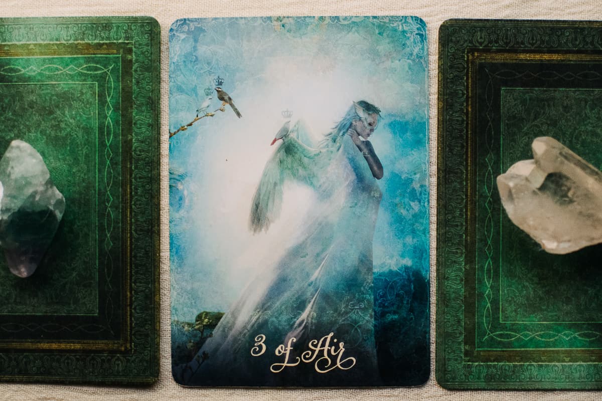 The Three of Air (Swords) tarot card between two other tarot cards in a spread. 