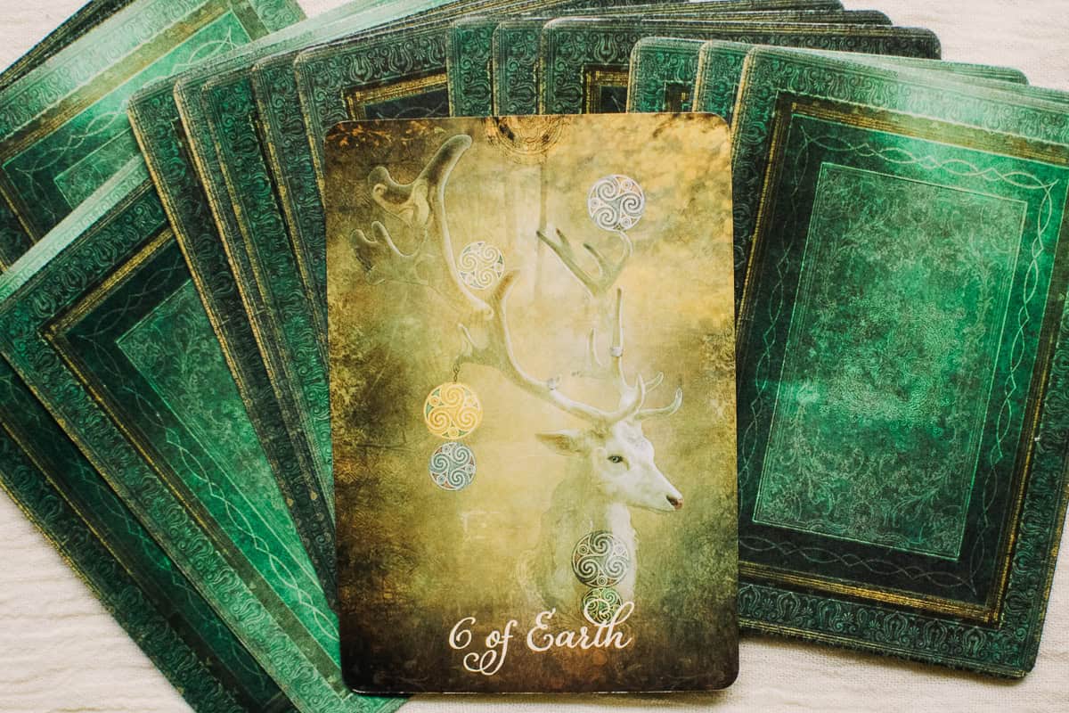 The Six of Earth (Pentacles) card depicted by a deer with 6 pentacles hanging off the horns.