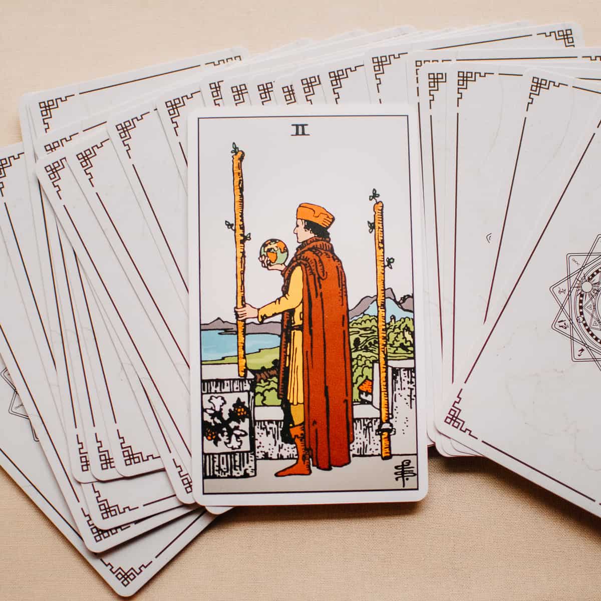 An individual looking out towards the horizon with a globe in his hand and two wands as depicted on the Two of Wands tarot card. 