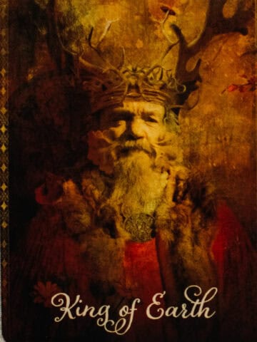 The King of Pentacles tarot card depicted by a King wearing a crown made of antlers.