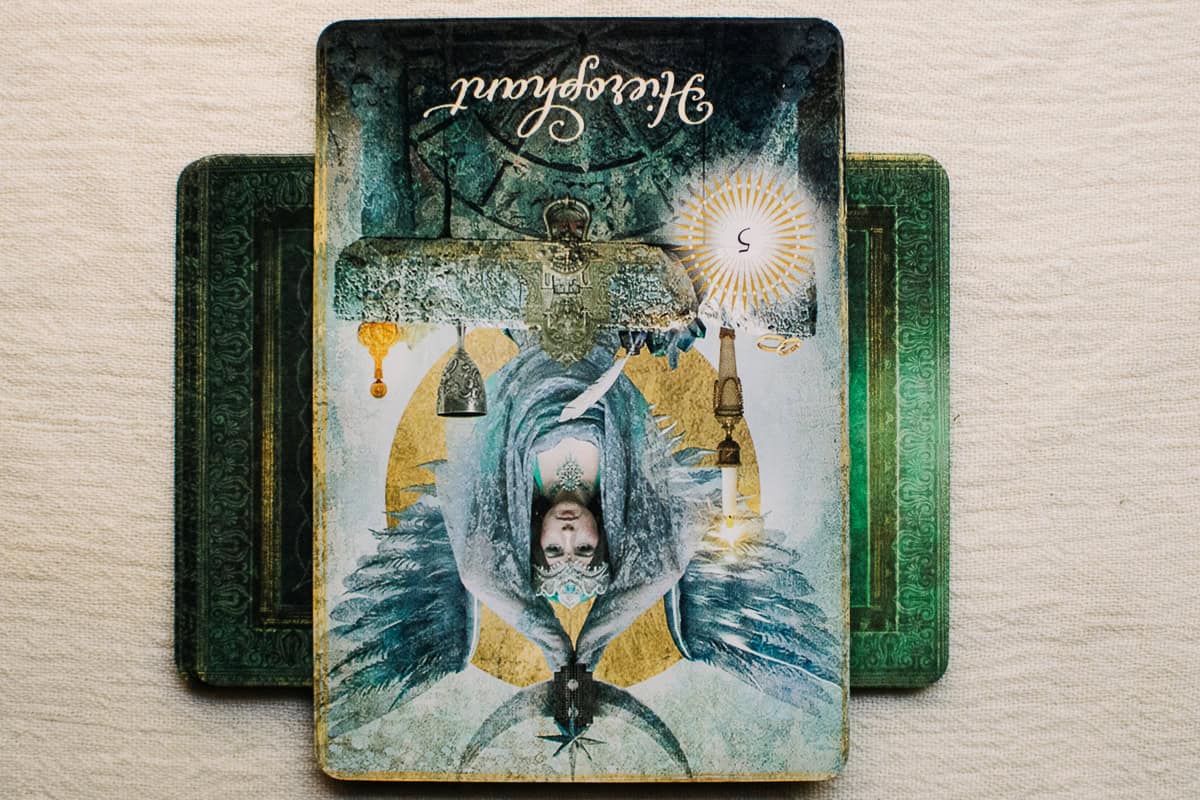 The Hierophant card in the reverse position on top of green deck of cards.