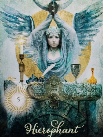 Hierophant card depicted by a woman with wings an hands above head holding a mezzaluna above her head.